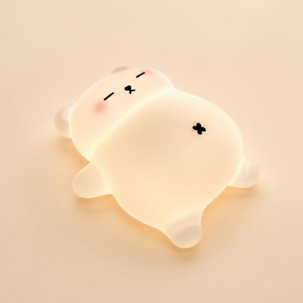 Veilleuse ourson Mimounou en silicone blanc, allumée, sur fond crème